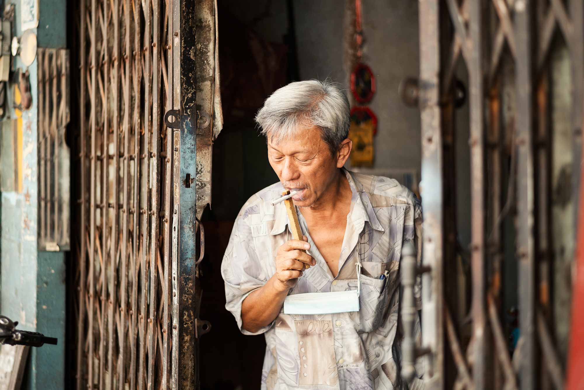 © Thilo Gögelein Fotografie // Mann mit Zigarette in einem Straßengeschäft in Bangkok, Thailand