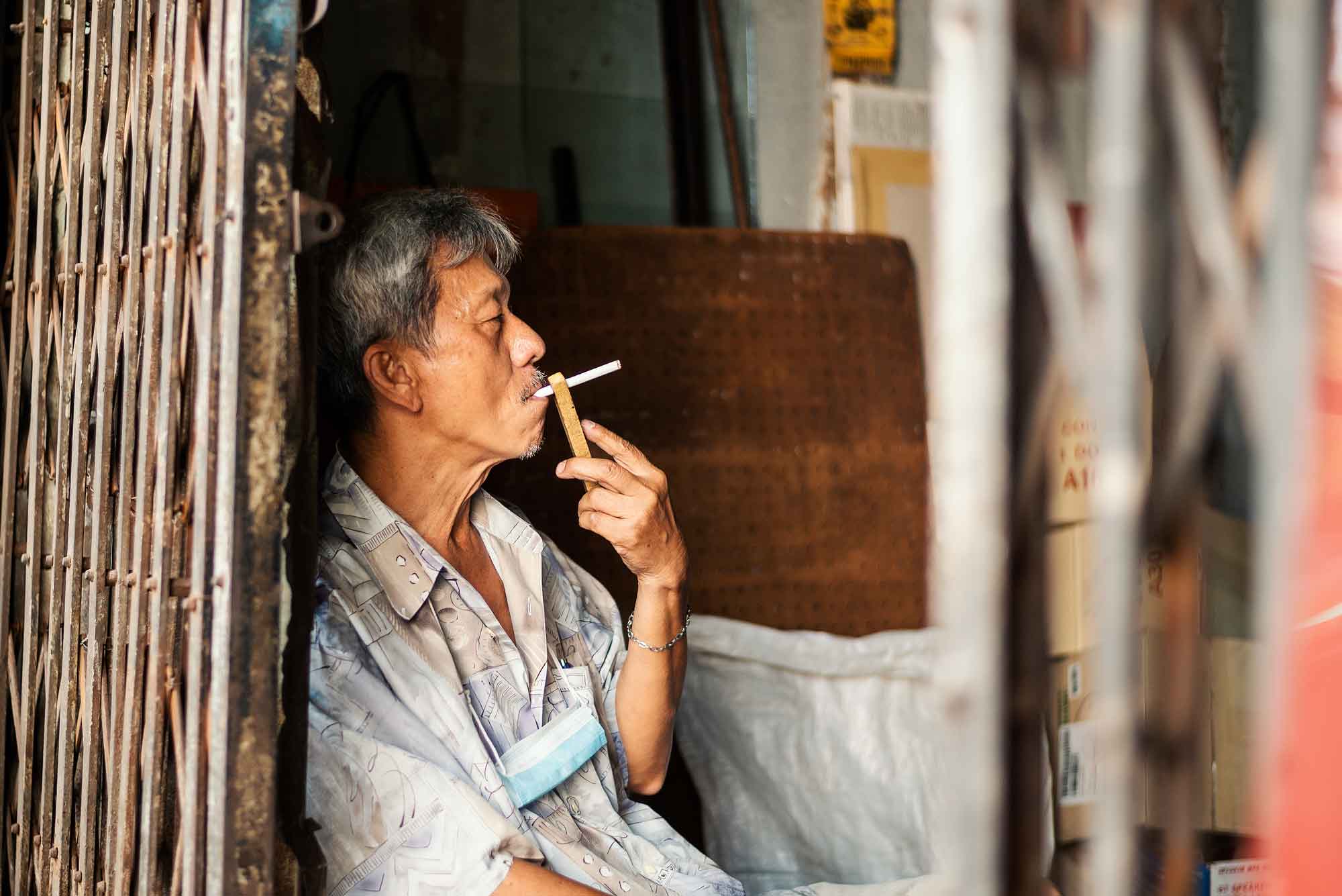 © Thilo Gögelein Fotografie // Mann mit Zigarette in einem Straßengeschäft in Bangkok, Thailand